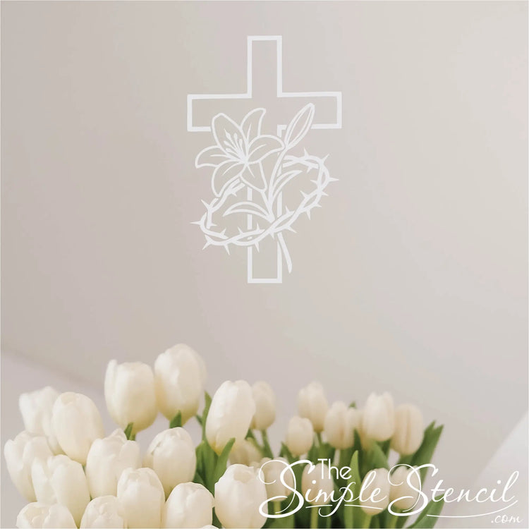 White silhouette wall decal of a Christian cross intertwined with a lily and crown of thorns wall decal, displayed in a modern home office above a desk with plants.