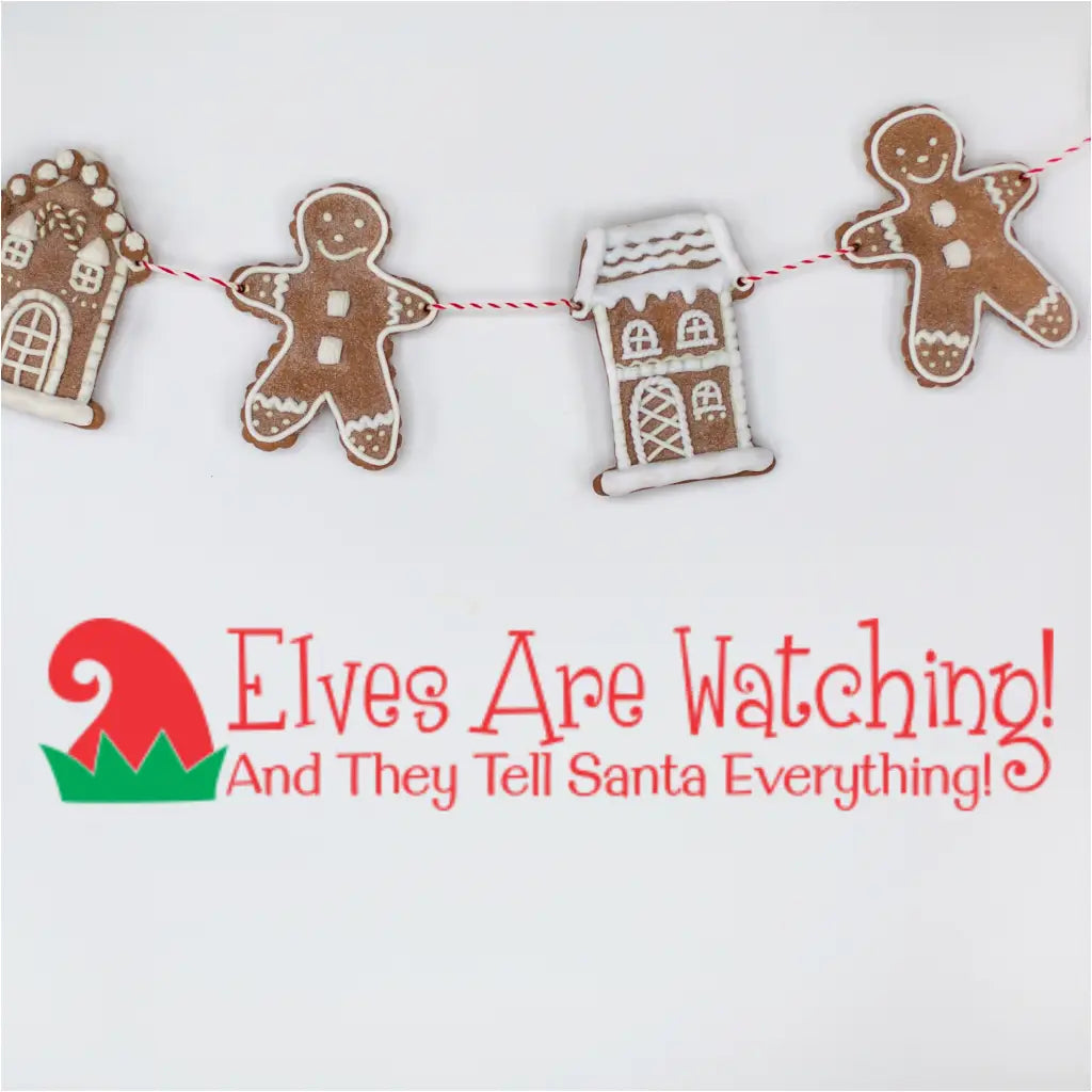 Lifestyle image featuring the red and green Christmas decal 'Elves Are Watching! And They Tell Santa Everything!' underneath a string of gingerbread men and gingerbread house cookies hung on a red and white baker's twine.