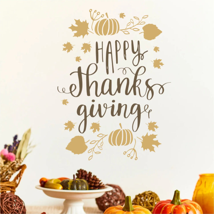 Tan and brown "Happy Thanksgiving" vinyl decal on a white wall above a buffet table. The decal has a whimsical script font surrounded by separate pumpkins and maple leaf vinyl stickers, showing custom fall decor arrangement.