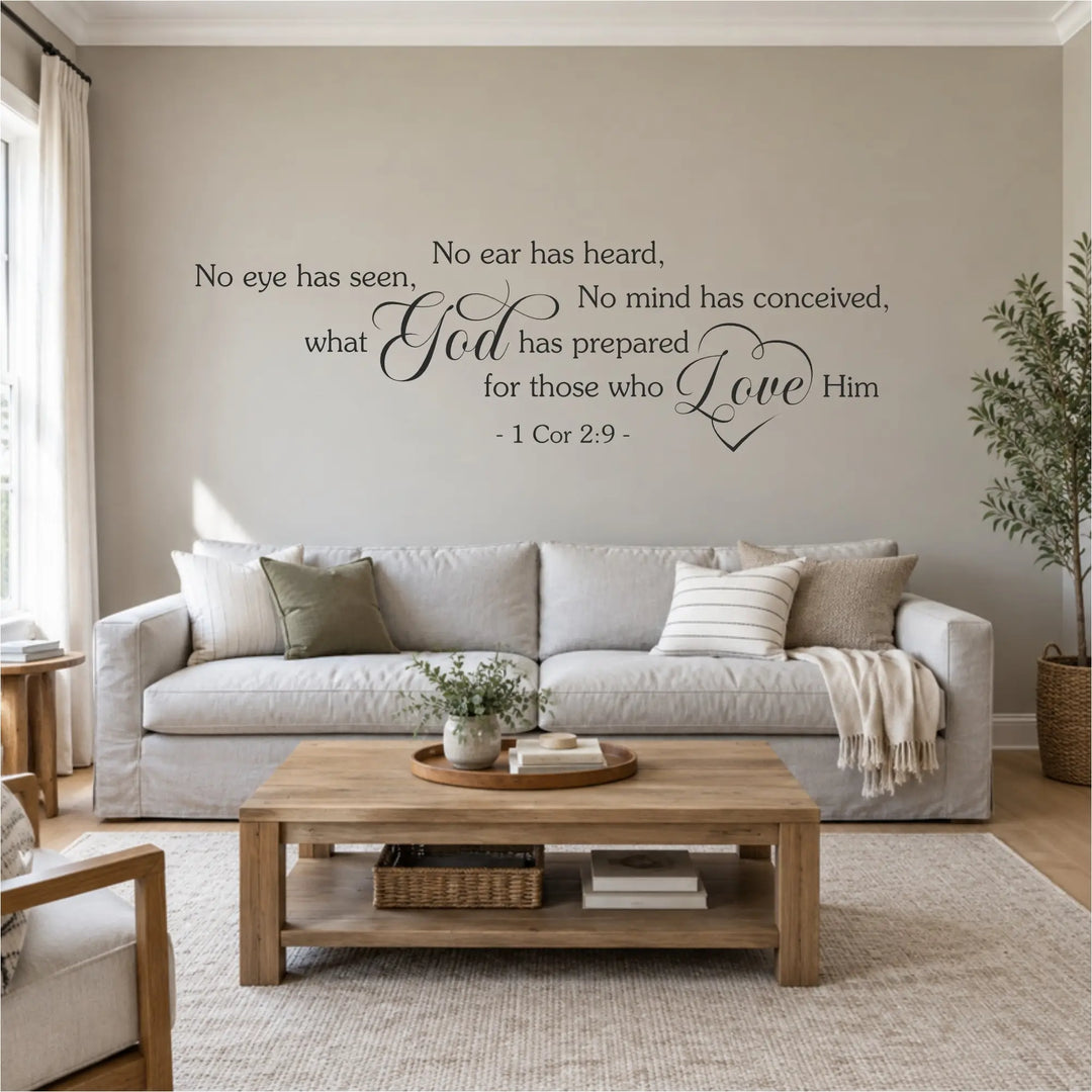 Charcoal 1 Corinthians 2:9 scripture wall decal reading No eye has seen, no ear has heard, with a flourished God and heart-wrapped Love, installed above a gray linen sofa in a bright farmhouse living room.