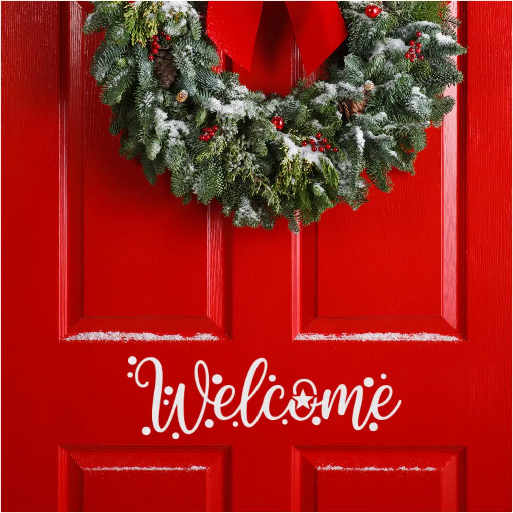 Close-up of a festive flocked evergreen wreath with pinecones, red berries, and a large red bow, hanging on a bright red door. A white "Welcome" decal with a star accent is visible below the wreath, perfect for holiday door decor.