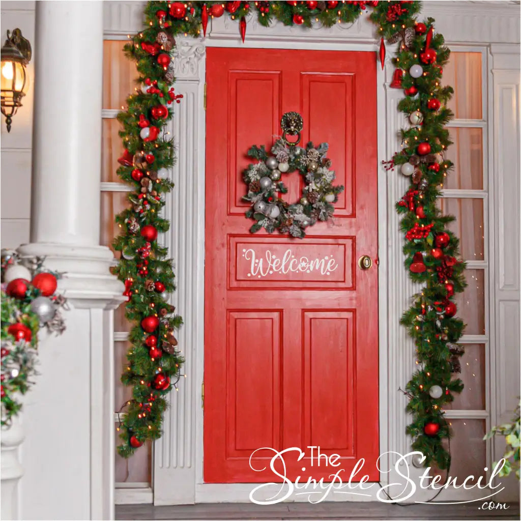 A vibrant red entry door adorned with a white "Welcome" decal, a frosted wreath with red and silver ornaments, and elaborate lit garlands featuring red and silver baubles around the doorframe and porch pillars, creating a warm holiday entrance.
