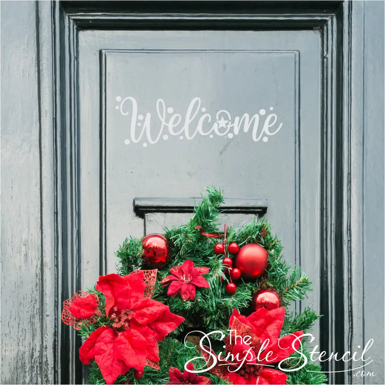 A chic gray entry door featuring a vibrant green holiday wreath adorned with large red poinsettias, glossy red ornaments, and red berries. A stylish white "Welcome" decal is positioned above the wreath, enhancing the festive door decor.