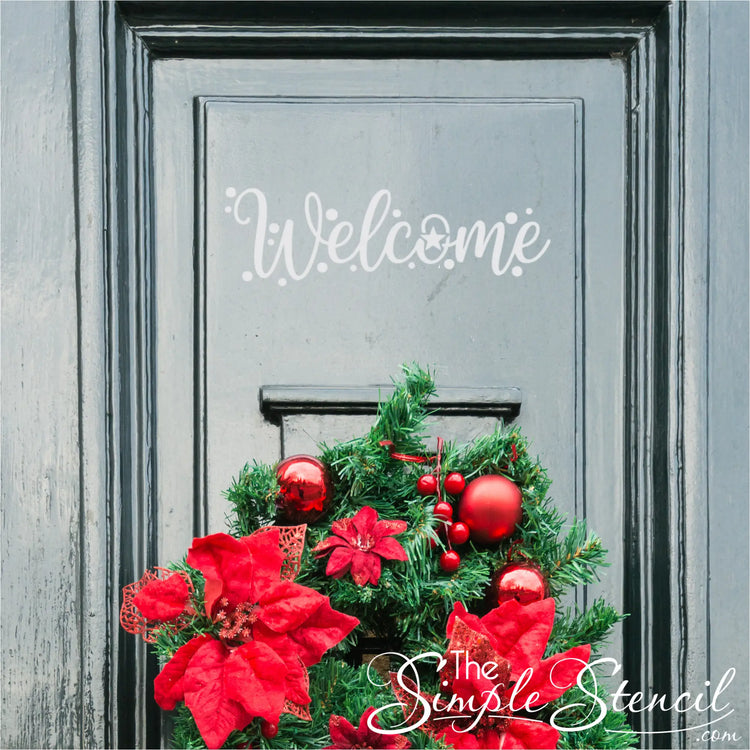 A chic gray entry door featuring a vibrant green holiday wreath adorned with large red poinsettias, glossy red ornaments, and red berries. A stylish white "Welcome" decal is positioned above the wreath, enhancing the festive door decor.