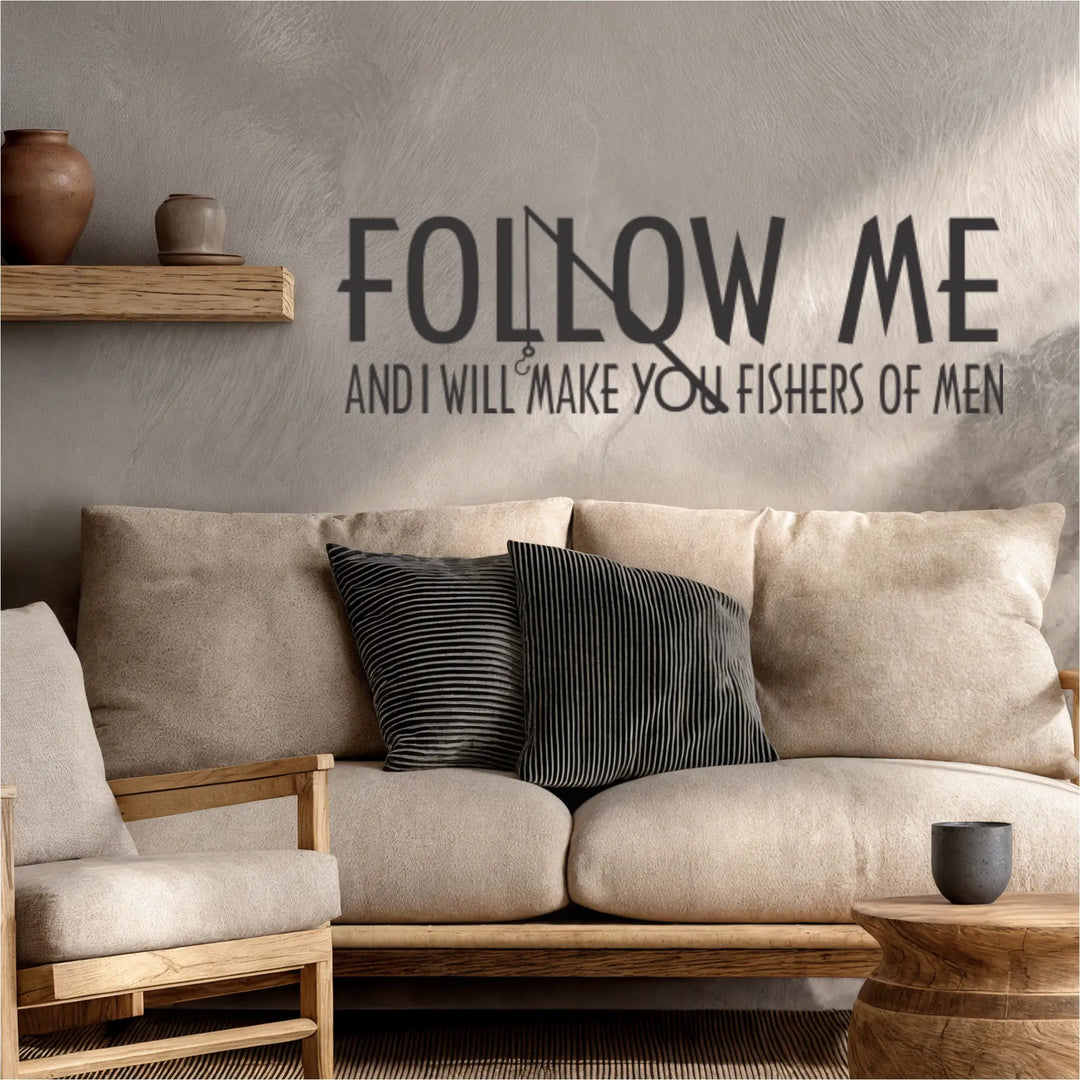 Dark charcoal 'Fishers of Men' scripture wall decal with an integrated fishing pole and hook graphic, styled in a modern lake house living room above a tan fabric sofa.