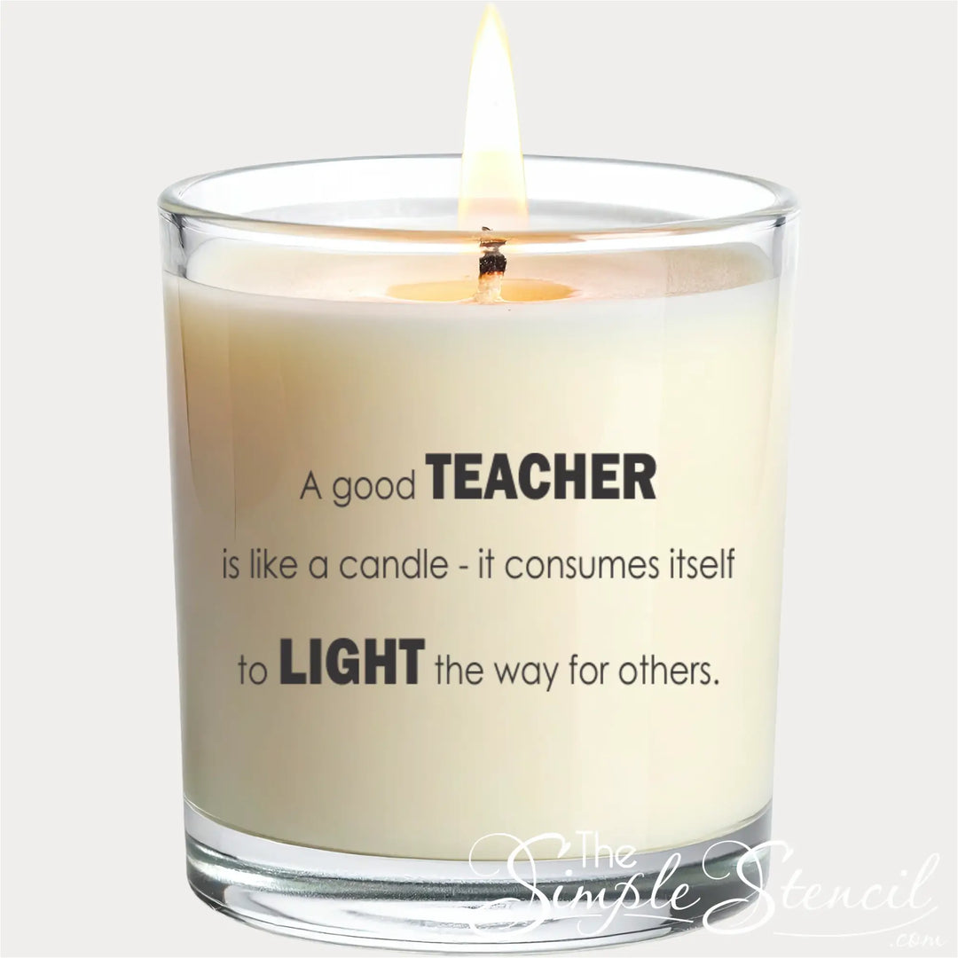 A close-up of a white scented candle in a clear glass jar with a lit flame. A black vinyl decal is applied to the front of the glass, featuring the quote "A good TEACHER is like a candle - it consumes itself to LIGHT the way for others." The words "TEACHER" and "LIGHT" are emphasized in a bold, modern typeface.