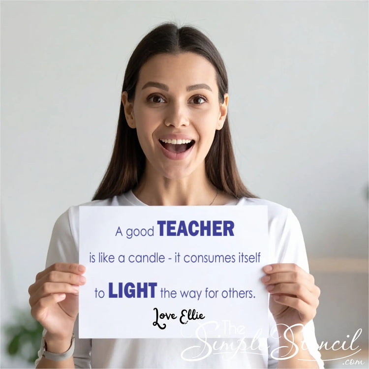 A smiling woman with long brown hair holds a white rectangular sign with both hands. The sign features the quote "A good TEACHER is like a candle - it consumes itself to LIGHT the way for others" in a modern sans-serif font. Below the quote, the text "Love Ellie" is written in an elegant black script.