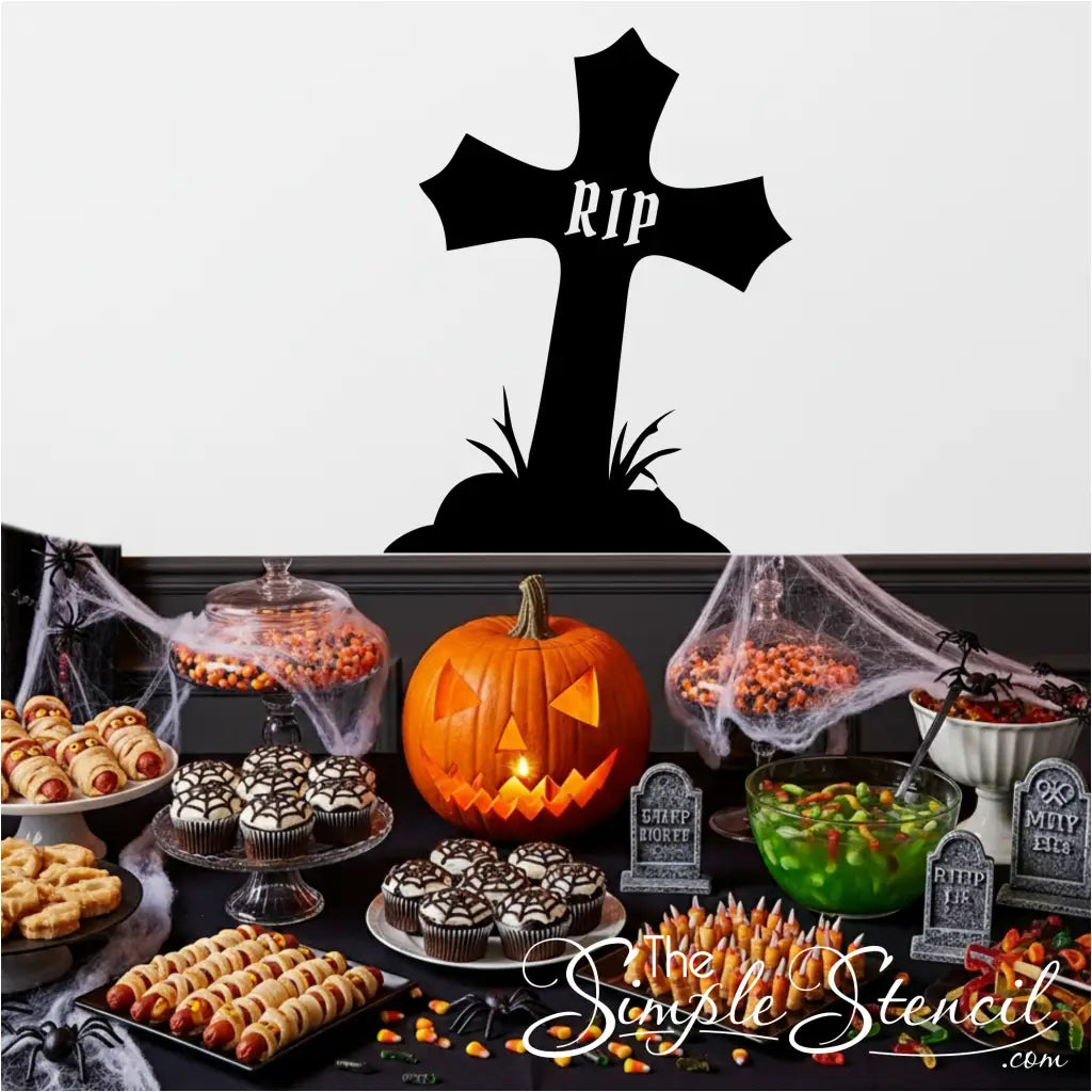 Halloween party table with spooky treats and a large RIP cross decal on the white wall behind it.