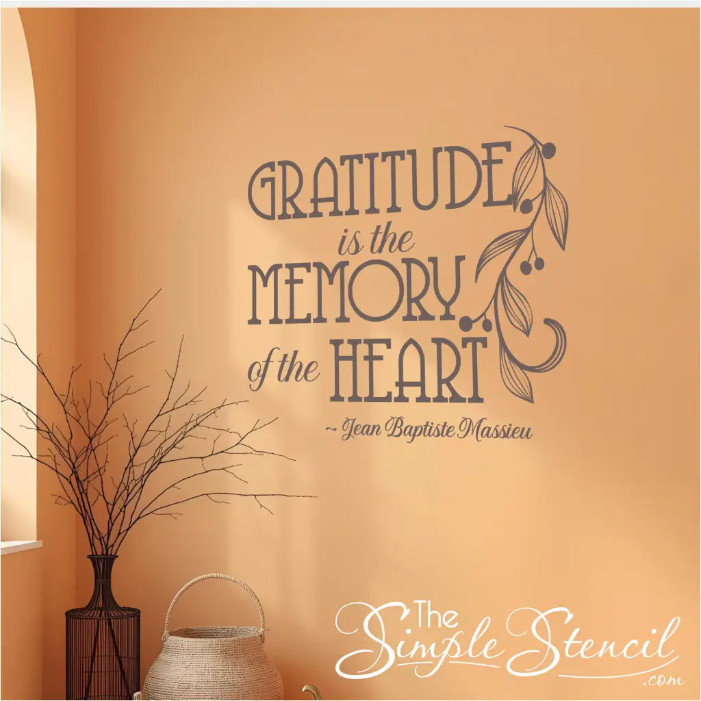A dark gray decal of the French quote "Gratitude is the Memory of the Heart" on a warm orange wall next to a window, showing its use in a room with fall colors.