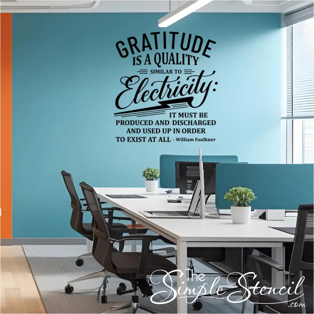 A black wall decal of the quote "Gratitude is a quality similar to electricity..." by William Faulkner, installed on a blue and orange accent wall in a modern corporate office space with multiple desks and computers.