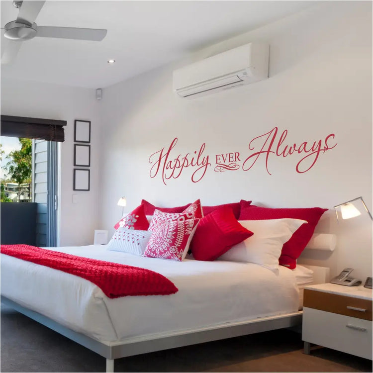 Red "Happily Ever Always" vinyl wall decal displayed above a modern bed with vibrant red and white patterned pillows and a red throw blanket, perfect for Valentine's Day bedroom decor.