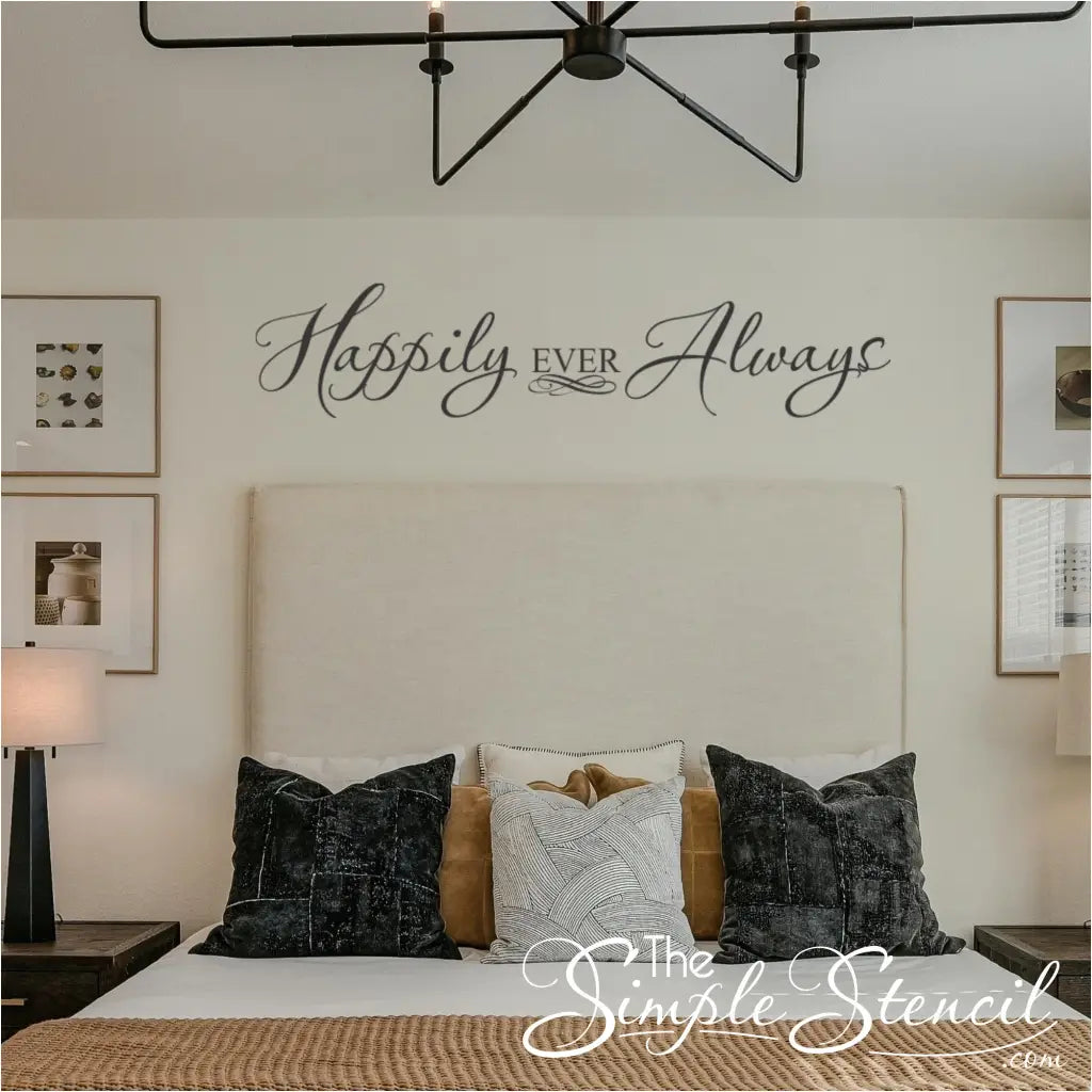 Elegant black script wall decal reading "Happily Ever Always" centered above a modern cream headboard in a master bedroom with decorative pillows and symmetrical lighting.