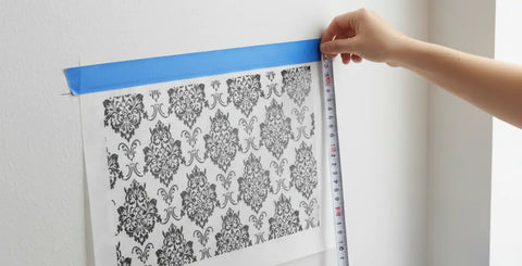 Using the hinge method with blue tape and a tape measure to level a large vinyl decal on a wall before application.