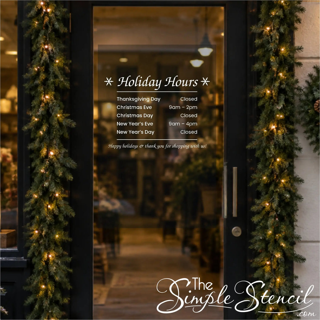 White Holiday Hours vinyl decal listing holiday dates and times on a glass shop door decorated with garland
