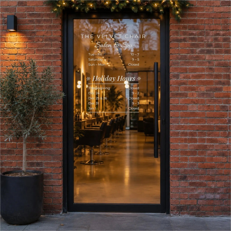 Holiday Hours add-on decal below a salon's name and business hours on a black-framed glass door