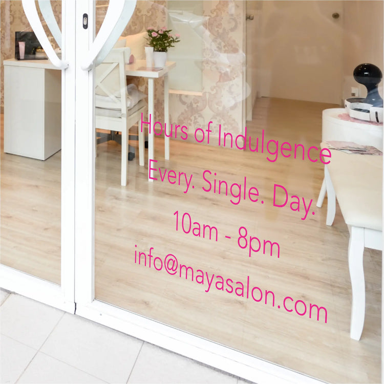 Chic salon window with a "Hours of Indulgence" decal and custom hours, complementing the elegant facade. By The Simple Stencil