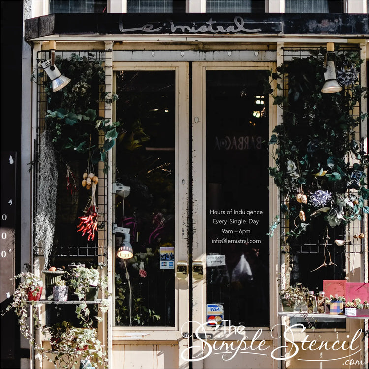 Cozy coffee shop window featuring a minimalist "Unleash Your Inner Indulgence: Every. Damn. Day." decal above steaming mugs and pastries, hinting at a daily coffee ritual to kickstart any adventure. By The Simple Stencil