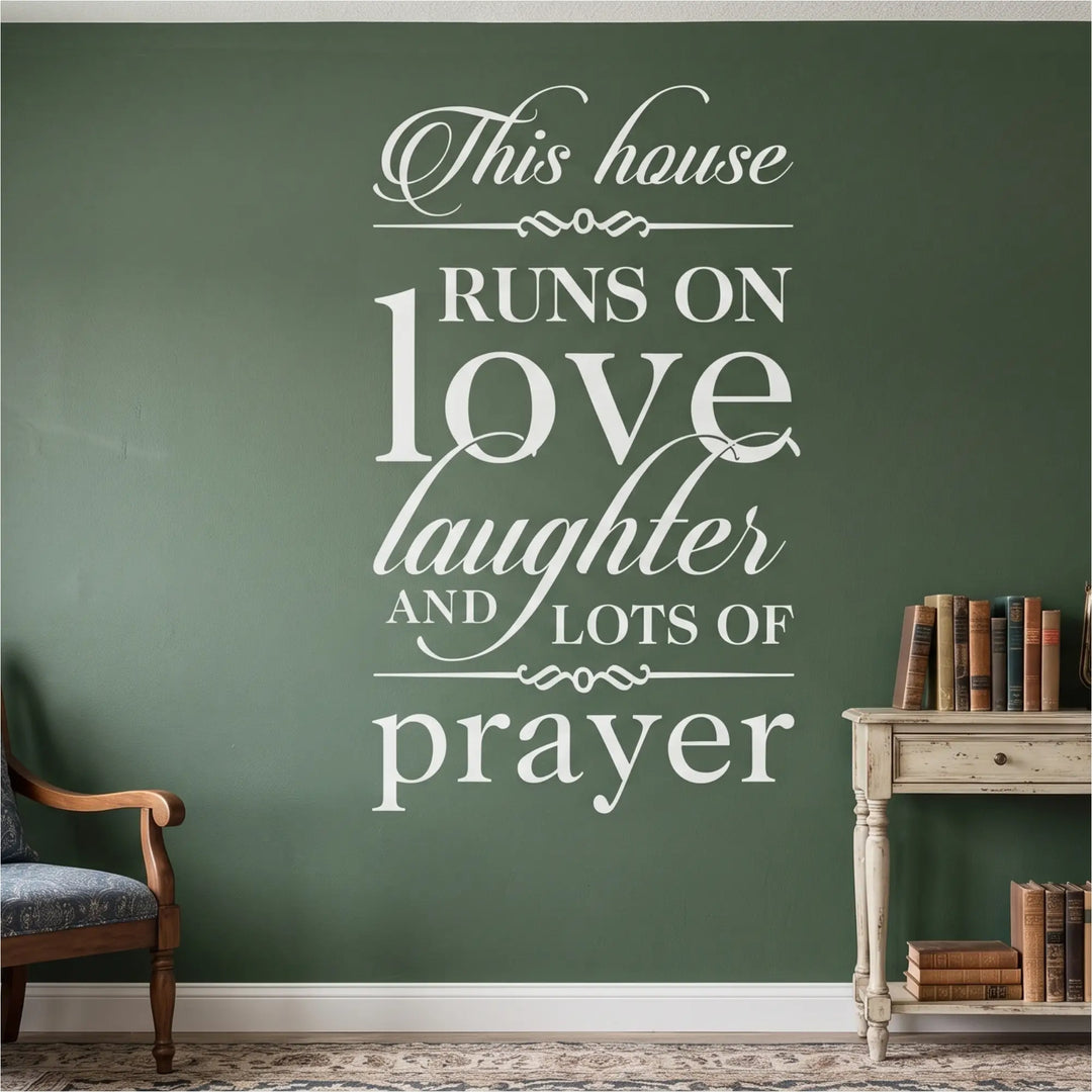 High-contrast white vinyl wall lettering featuring the complete 'This house RUNS ON love laughter AND LOTS OF prayer' scripture coordination design applied flawlessly to a deep forest green textured accent wall above a traditional console table with antique books, providing a sacred, painted-on anchor point for the domestic church.