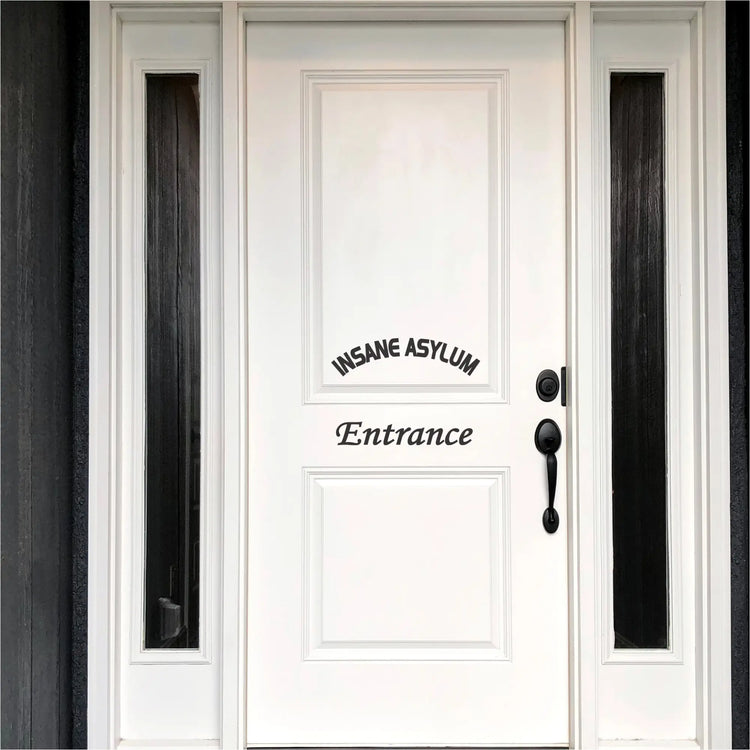 A black "Insane Asylum Entrance" vinyl decal on a white front door, positioned to look like a welcome sign.