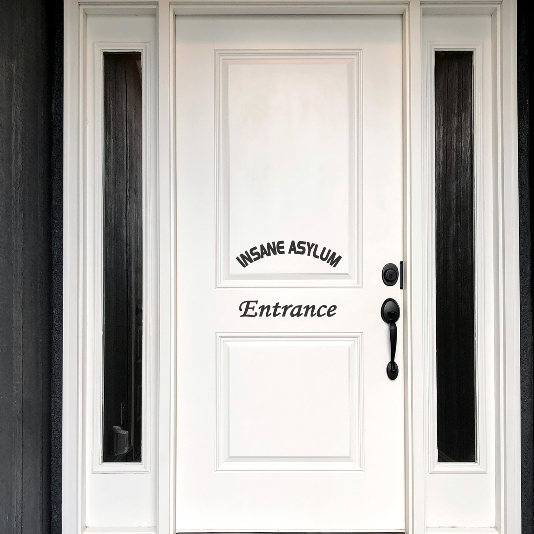 A black "Insane Asylum Entrance" vinyl decal on a white front door, positioned to look like a welcome sign.