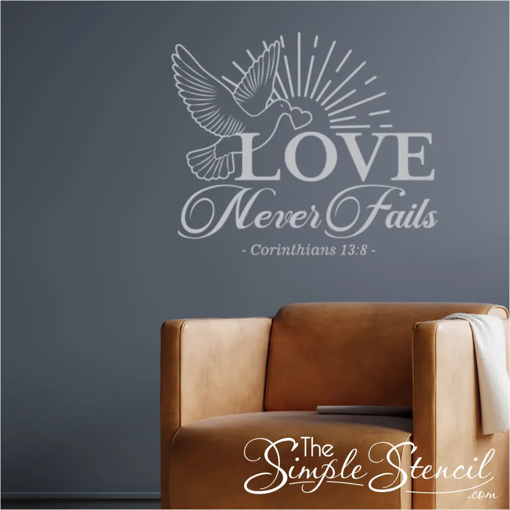 Love Never Fails Wall Decal with dove flying with heart in it's beak, shown in white over a chair on a blue wall. 