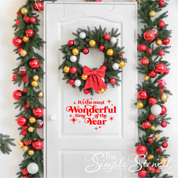 Removable Christmas decal 'It's the Most Wonderful Time of the Year' displayed on a door, surrounded by festive garland and a wreath. Great for renters or apartment decorating as it leaves no residue. Simple peel-and-stick holiday design.