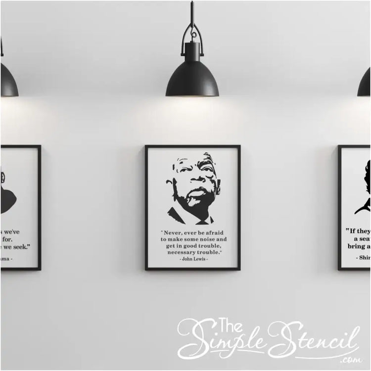 Gallery wall display featuring three framed prints under pendant lighting, with the center poster showcasing the John Lewis silhouette and full "Good Trouble" quote.
