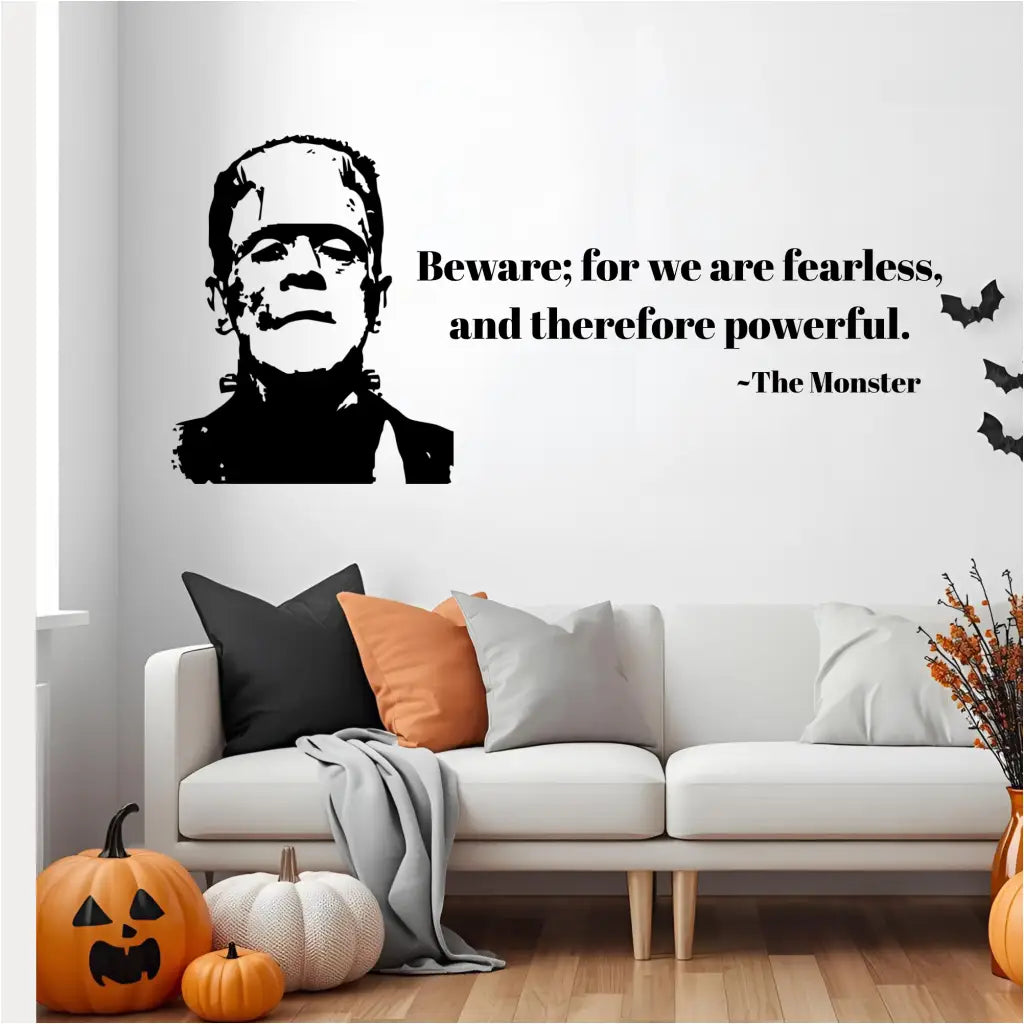  A living room scene with a black wall decal of the Monster of Frankenstein and a quote in black text that reads, "Beware; for we are fearless, and therefore powerful. ~The Monster." The decal is placed above a white couch with decorative pumpkins on the floor.