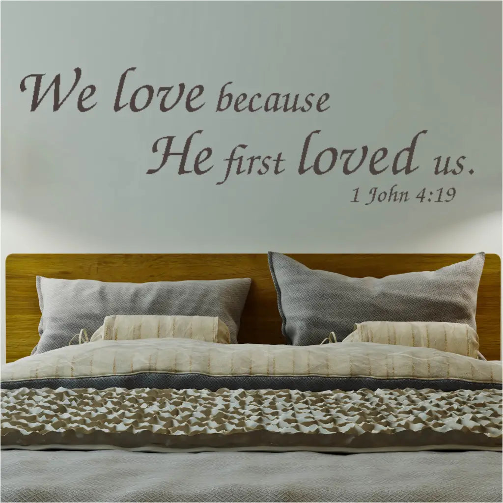 "We Love Because He First Loved Us" Bible Verse Wall Decal above a Bed. Creates a warm and inviting atmosphere in your Christian home decor.