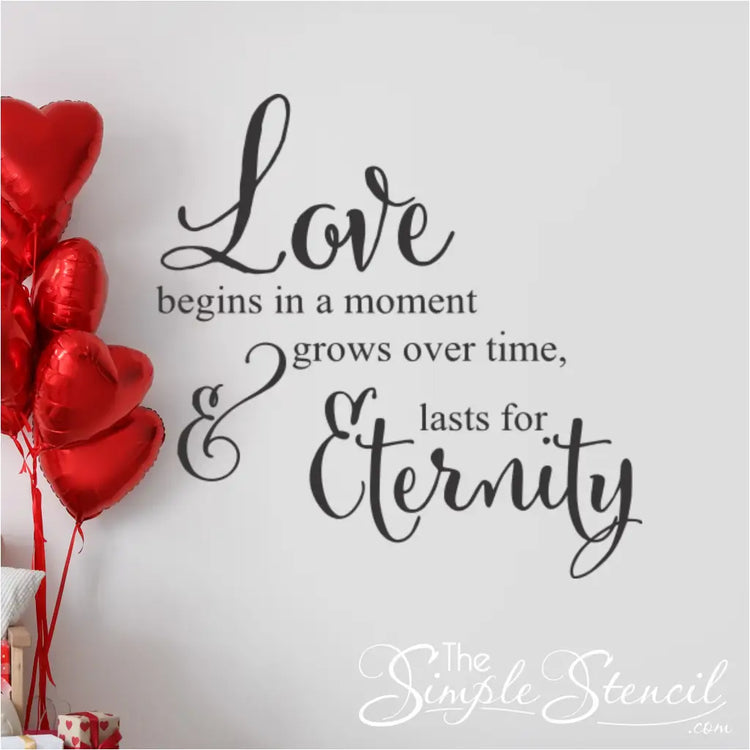 Romantic bedroom surprise featuring red heart-shaped balloons next to a "Love begins in a moment" wall decal, ideal for Valentine's Day or anniversary gift ideas.