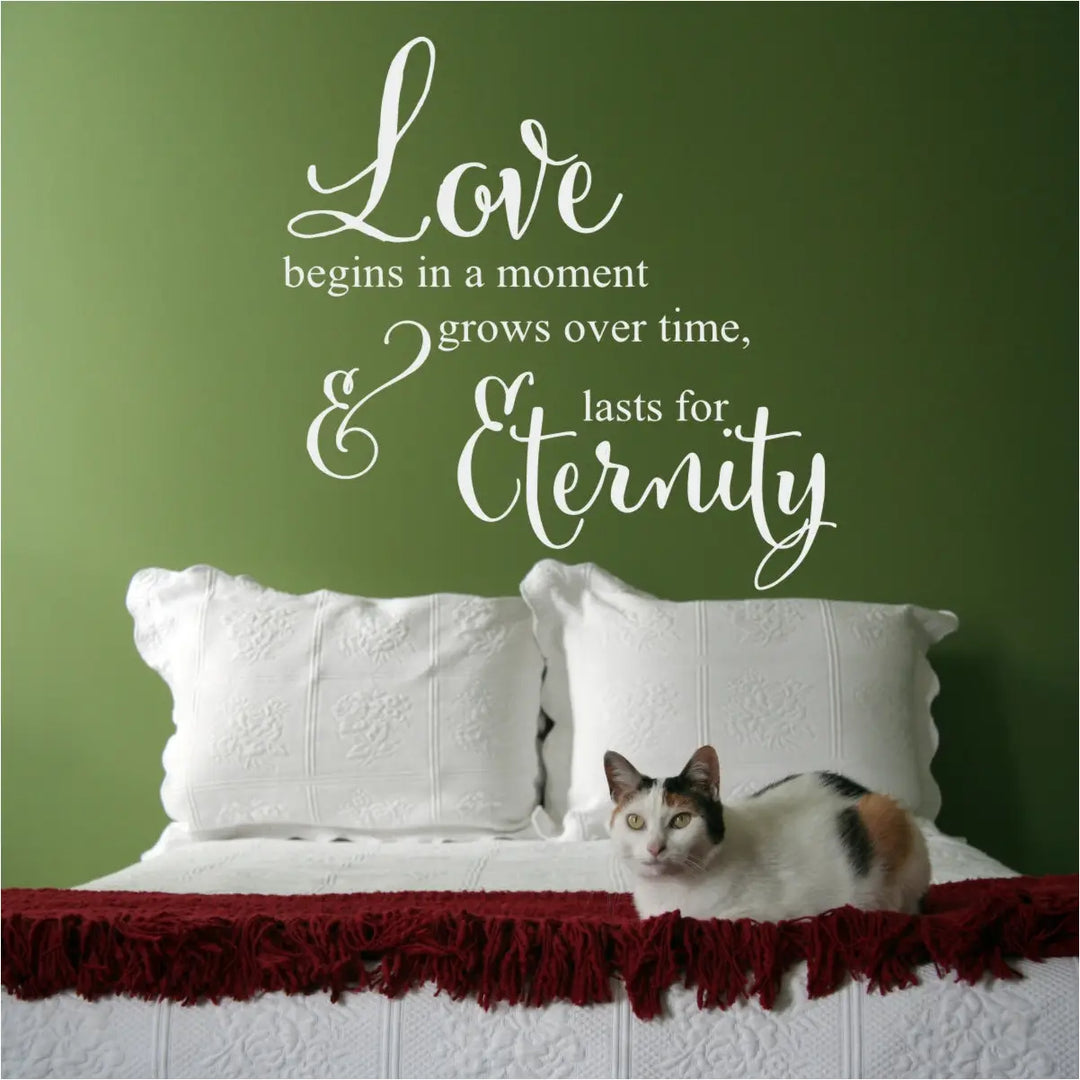 White "Love begins in a moment" wall decal prominently displayed on a vibrant green bedroom wall above a white bed with a red fringed throw blanket.