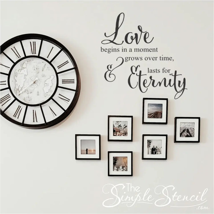 Black vinyl wall quote centered in a gallery wall of square photos next to a large Roman numeral wall clock, creating a sentimental family room display.