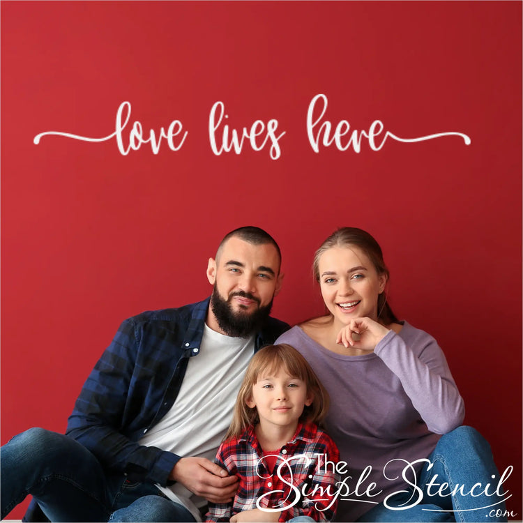 Wall decal featuring 'Love Lives Here' with a flourish design above a family posing for photo.