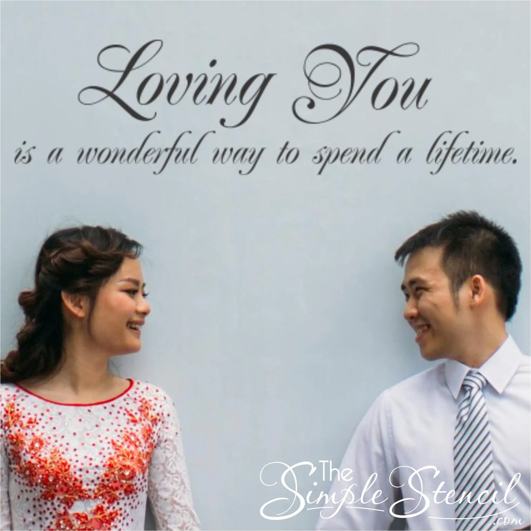 A happy couple smiling at each other in front of a light blue wall featuring the romantic vinyl quote "Loving You is a wonderful way to spend a lifetime."