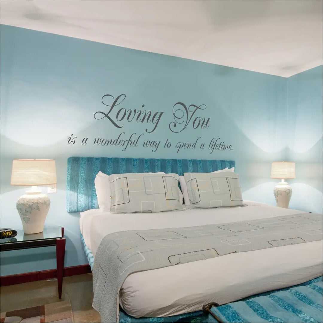 Elegant grey wall decal reading "Loving You is a wonderful way to spend a lifetime" centered on a light blue master bedroom wall above a modern tufted headboard.