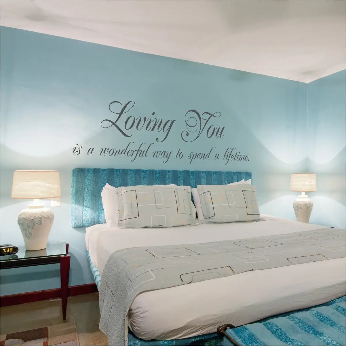 Elegant grey wall decal reading "Loving You is a wonderful way to spend a lifetime" centered on a light blue master bedroom wall above a modern tufted headboard.