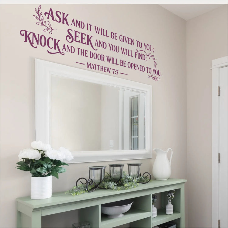 Matthew 7:7 portable church wall lettering in eggplant purple finish arranged over a large white-framed mirror and light sage console table in a bright home foyer.