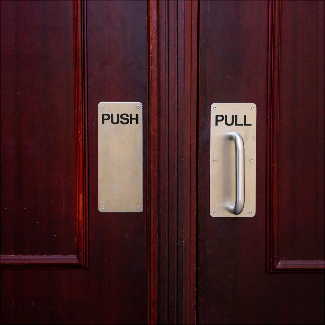 Premium silver stainless steel door pull plate on a dark mahogany corporate office entrance door, printed with PULL in a clean black sans-serif font for professional reception areas.