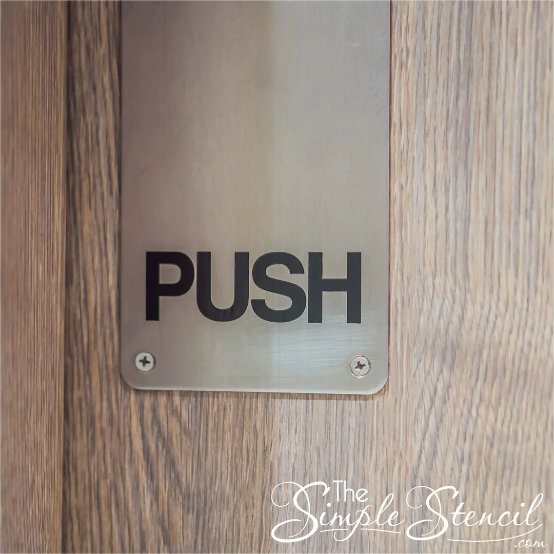 Close-up of a modern light-oak interior office door showing a silver metal vertical push plate printed with "PUSH" in bold black letters.