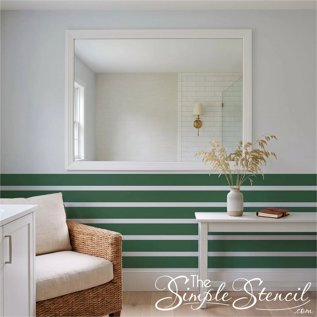 A styled interior scene with a large white-framed mirror on a pale gray wall above a green-and-white striped wainscoting. The green stripes were created easily using simple stencil peel and stick decals in 4" high strips. 