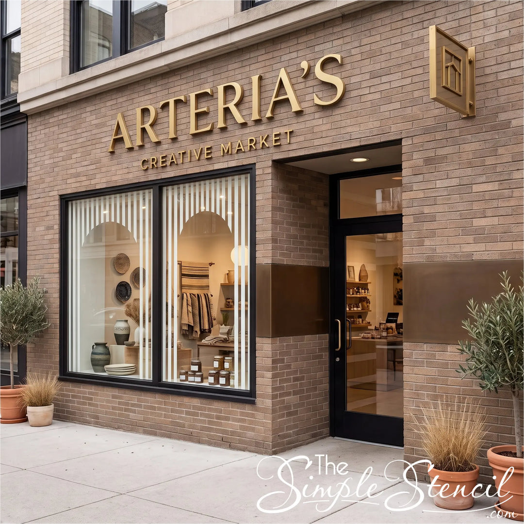 Arteria's Creative Market storefront on a brick building, featuring large gold lettering, black-framed windows and door, and potted plants on the sidewalk. White striping on windows supplied by Simple Stencils to create a modern inviting storefront. 