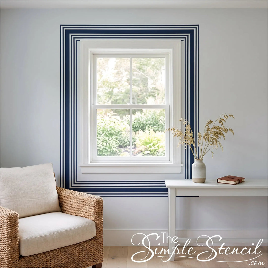 A styled interior room scene showing a white-framed window with bold navy blue decorative border stripes on the wall. The blue stripes were created using Simple Stencil peel and stick vinyl strips in the 2" and 3/4" sizes. 