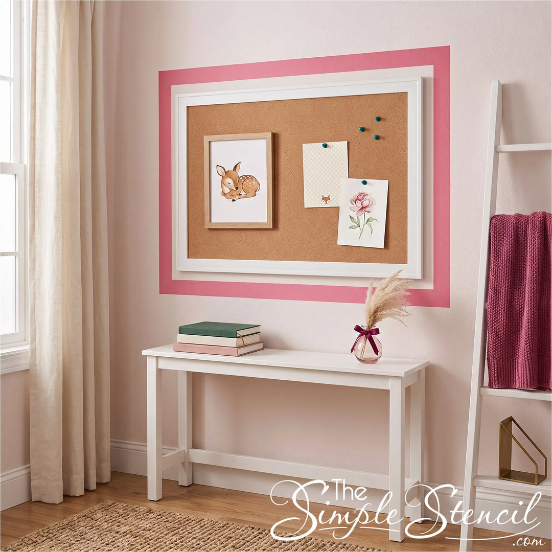 A framed cork bulletin board with a white frame and pink border hangs on a light pink wall above a white console table. The single pink stripe upgrades the space in an easy peel and stick method that is 100% removable. 