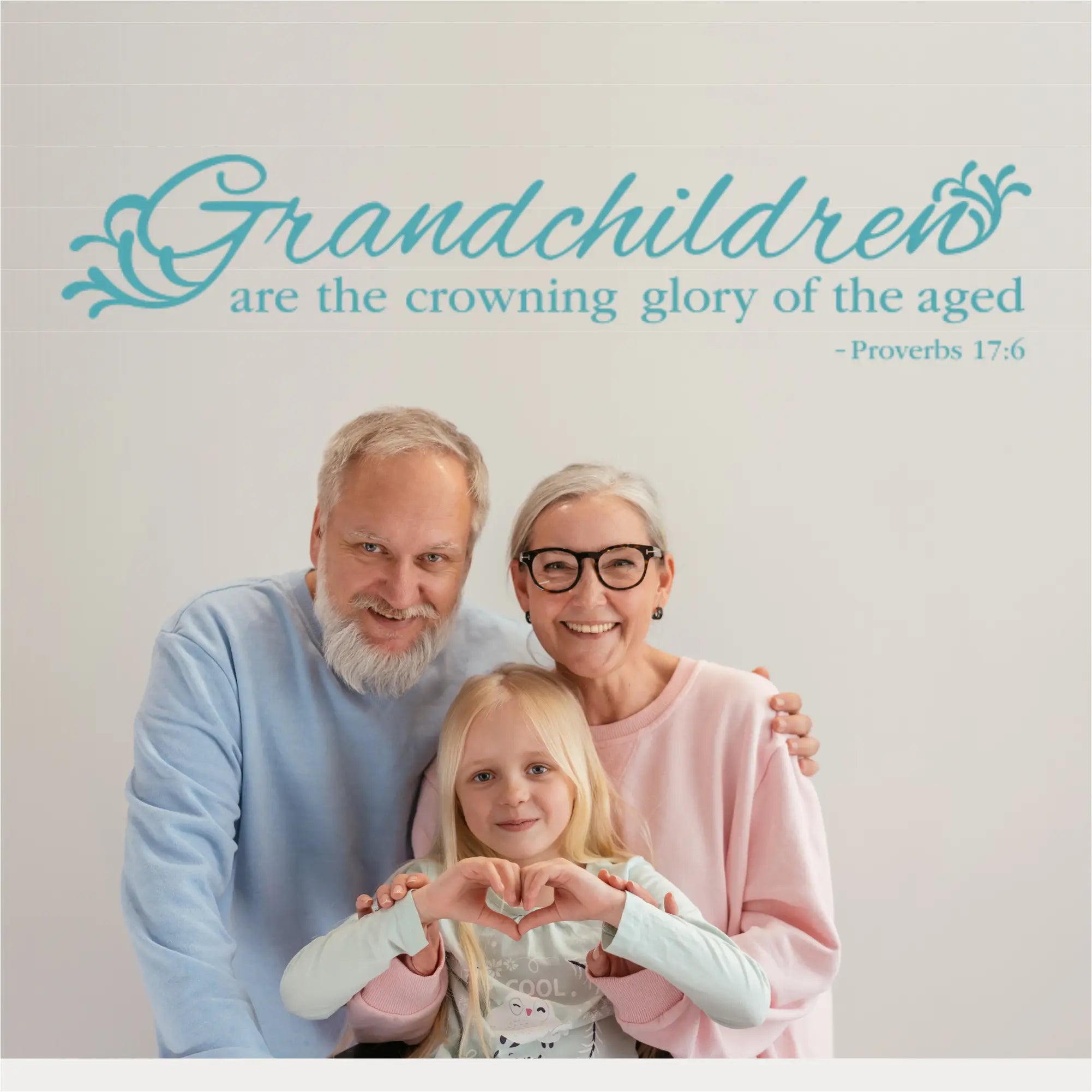 A teal blue scripture wall decal for Proverbs 17:6 positioned above a grandfather and grandmother hugging their young granddaughter, illustrating a legacy of love and Christian family decor.