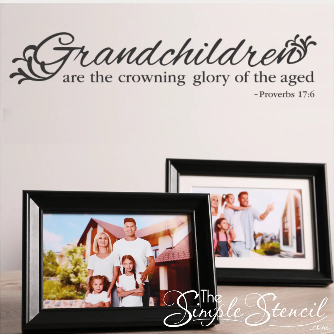 Black vinyl Proverbs 17:6 wall decal that reads 'Grandchildren are the crowning glory of the aged,' styled on a white wall above two black picture frames containing family photos.