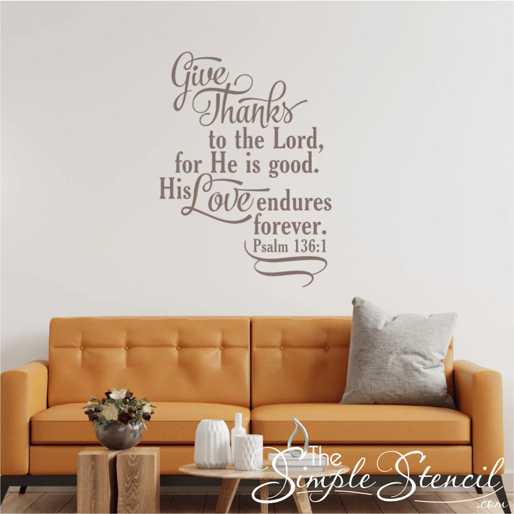 Psalm 136:1 "Give Thanks to the Lord" vinyl decal in taupe, installed above a modern orange living room couch with throw pillows.