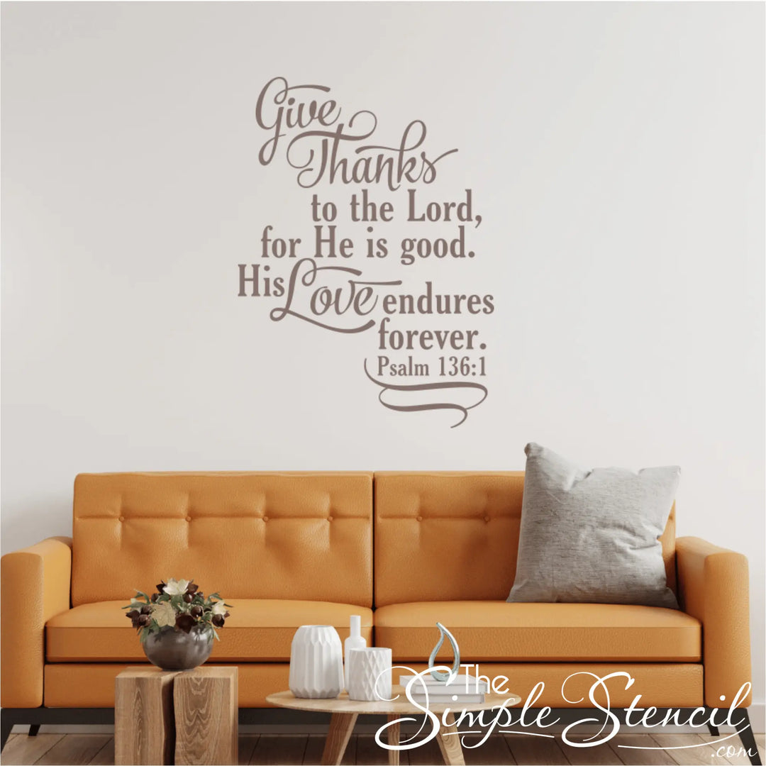 Psalm 136:1 "Give Thanks to the Lord" vinyl decal in taupe, installed above a modern orange living room couch with throw pillows.
