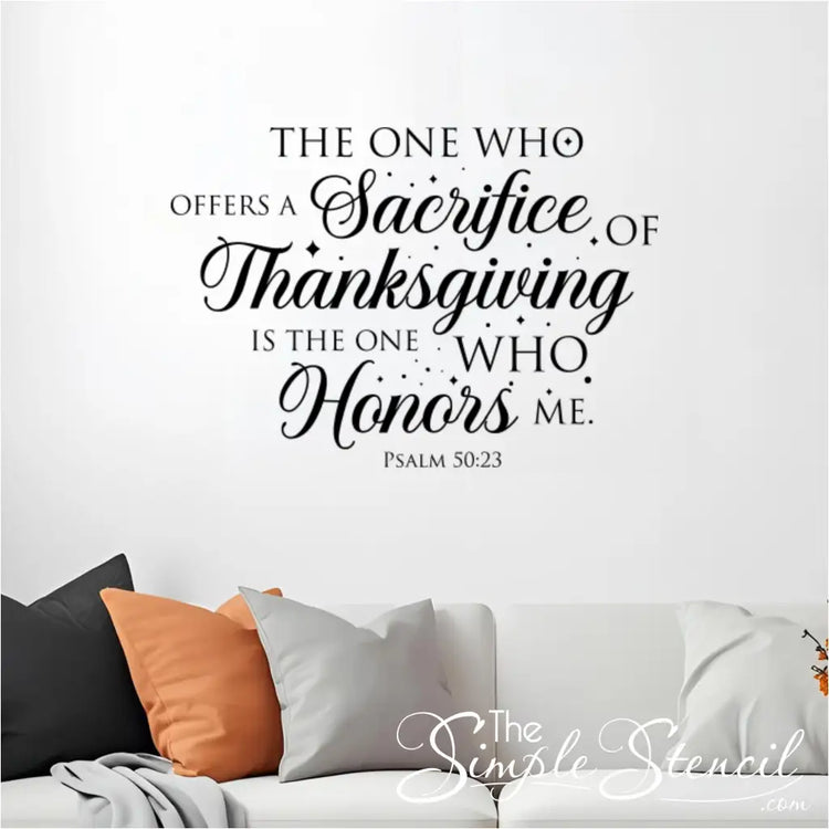 The black Psalm 50:23 'Sacrifice of Thanksgiving' wall decal is shown in a living room above a white sofa with orange, black, and gray fall-colored pillows.