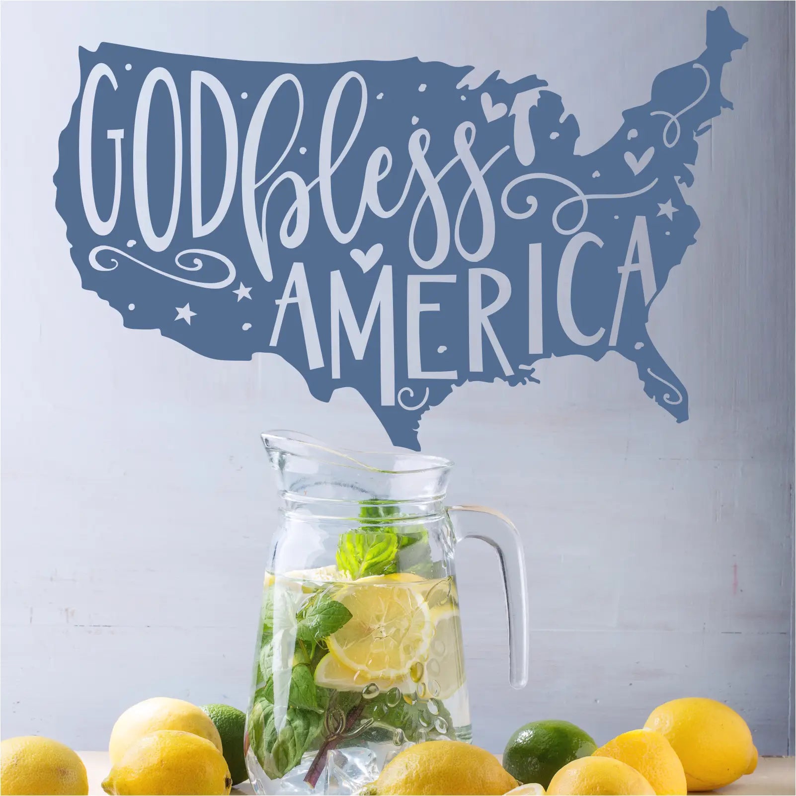 Clear glass pitcher with water lemon slices and mint next to removable whimsical god bless america usa map wall decal