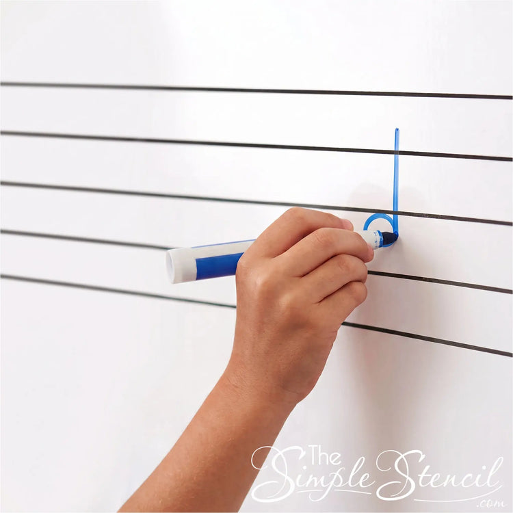 A detailed close-up square photograph focusing tightly on a portion of the sharp black applied reusable vinyl G-clef and staff lines on a clean whiteboard. A student's hand, holding a blue dry-erase marker, is actively drawing a quarter note on the second staff line (G), demonstrating the product's function for interactive music notation and practice.